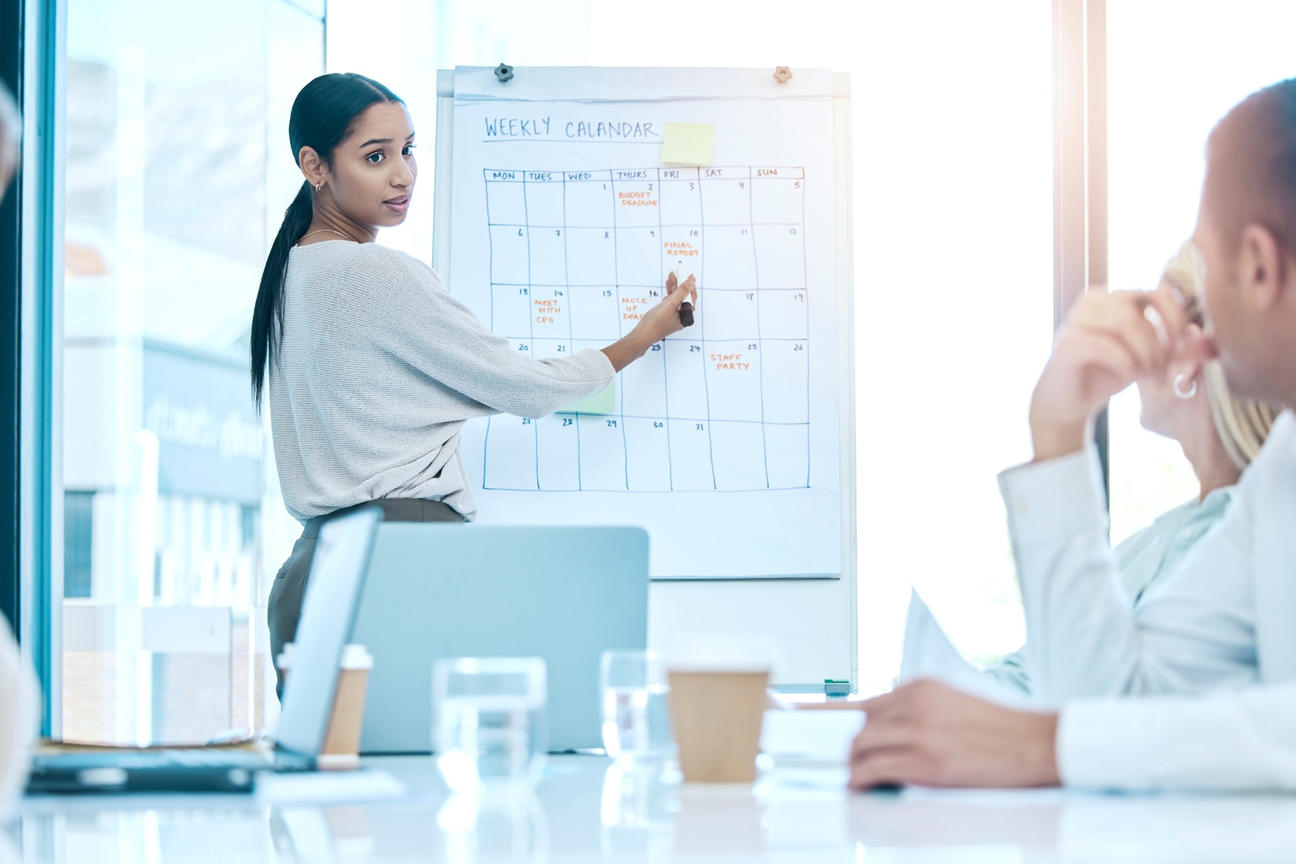 two workers look over a whiteboard calendar