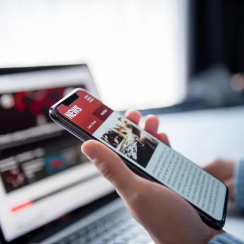 Person's hand holding a mobile phone reading a news website.